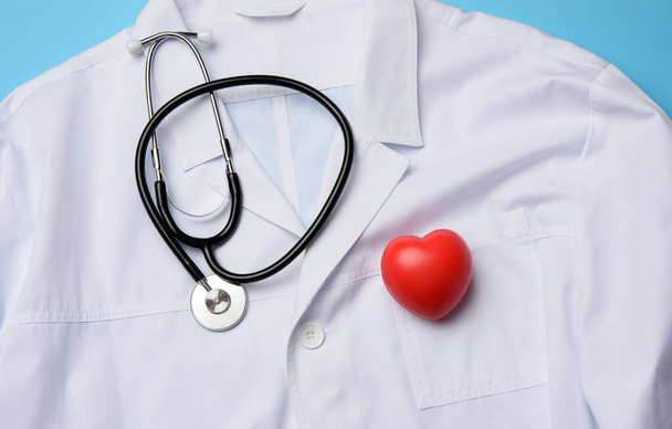 червоне серце і чорний стетоскоп лежать на білій медичній сукні, вид зверху
 - Фото, зображення