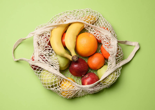 ripe fresh fruits in a textile string bag on a green background, top view - Foto, Imagen