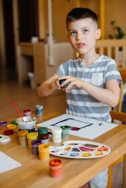 A cute little boy is playing and painting in his room. Recreation and entertainment. Stay at home - Foto, afbeelding