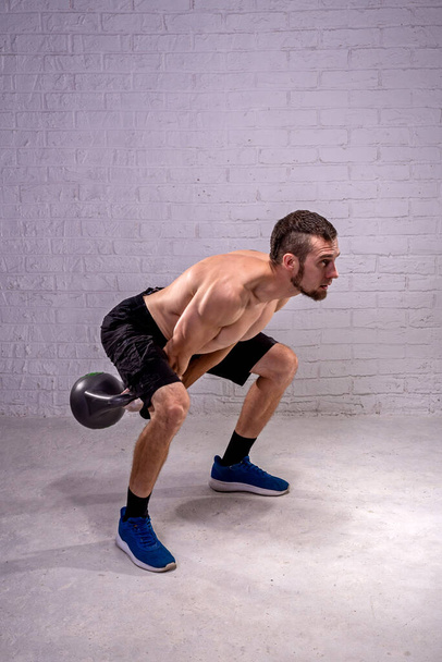 Fitness with kettlebell, man trains with kettlebell on gray background. Active lifestyle, sports. - Foto, Imagen