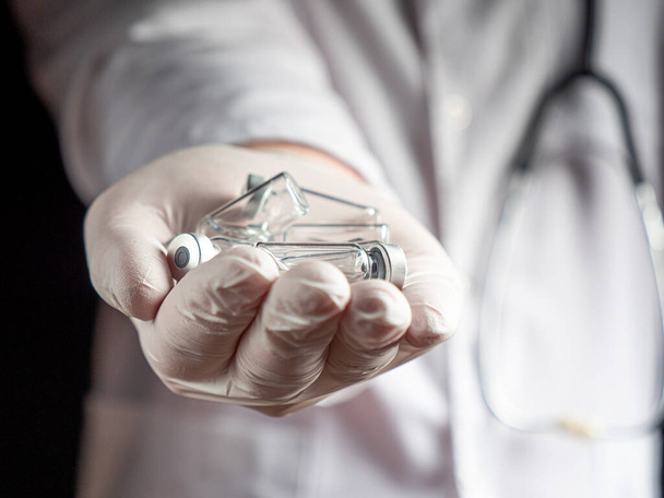 Nuoren lääkärin ojennetussa kädessä on lasinen rokotepullo. valikoiva keskittyminen ojennettuun käsivarteen lasisilla injektiopulloilla rokotetta nestettä - Valokuva, kuva