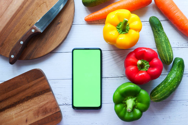legumes frescos, placa de corte e telefone inteligente na mesa  - Foto, Imagem