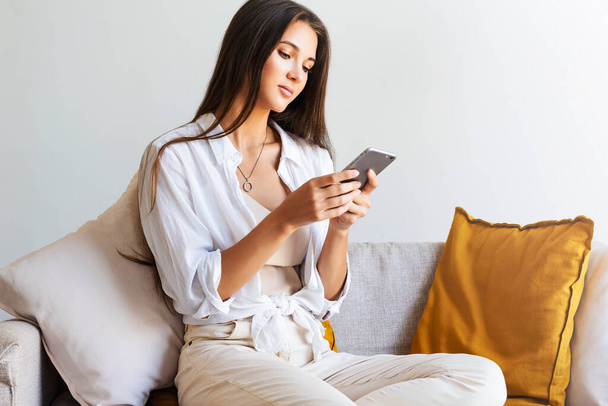 Жінка розслабляється вдома, використовуючи смартфон, щоб писати повідомлення, ділитися фотографіями, спілкуватися з друзями
 - Фото, зображення