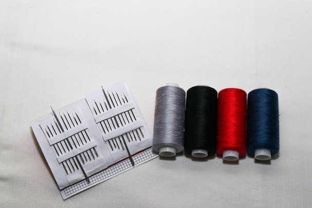 Gekleurde draden en naalden. Alles wat je nodig hebt voor het naaien. Meerdere spoelen draad. Scherpe naalden.Rode, zwarte, grijze en blauwe draadspoelen geïsoleerd op witte achtergrond - Foto, afbeelding
