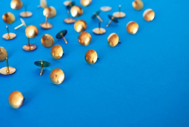 A group of golden thumb tacks on a blue surface. - Фото, зображення