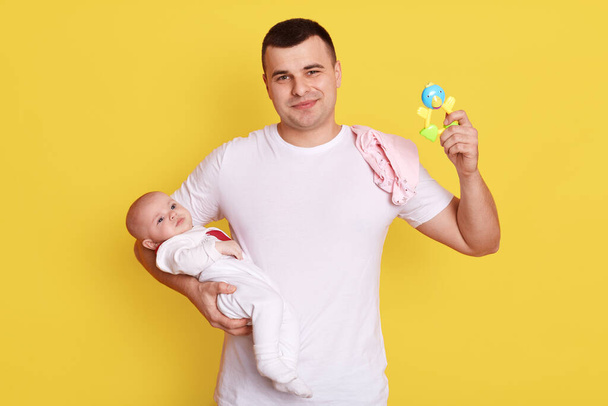Happy father with little baby daughter at home playing together, young dad with rattle taking care with her daughter while posing isolated over yellow background. - Fotoğraf, Görsel