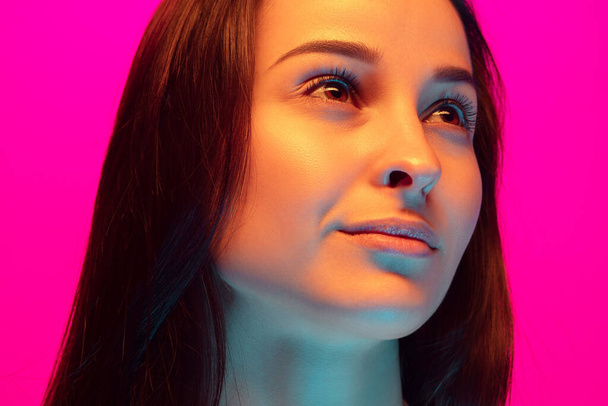 Caucasian beautiful womans portrait isolated on pink studio background in multicolored neon light - 写真・画像
