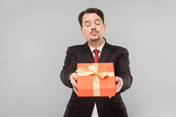 Business man holding red gift box. Send air kissing. Indoor, studio shot, isolated on gray background - Fotoğraf, Görsel