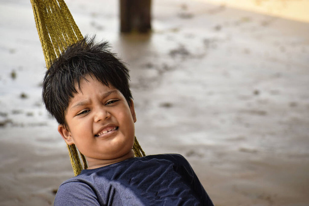 усміхнений південноазіатський хлопчик відпочиває в гамаку
 - Фото, зображення