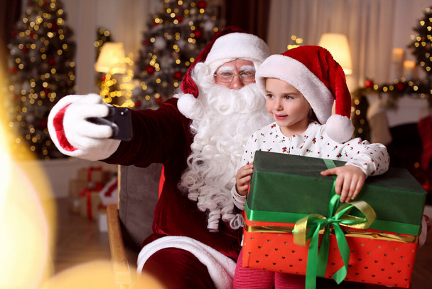 Santa Claus and little girl taking selfie in room decorated for Christmas - Foto, Imagen