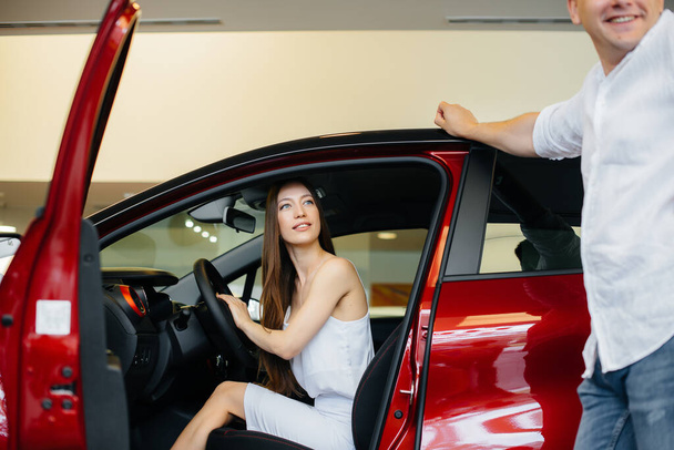A happy young couple chooses and buys a new car at a car dealership. Buying a new car - Zdjęcie, obraz