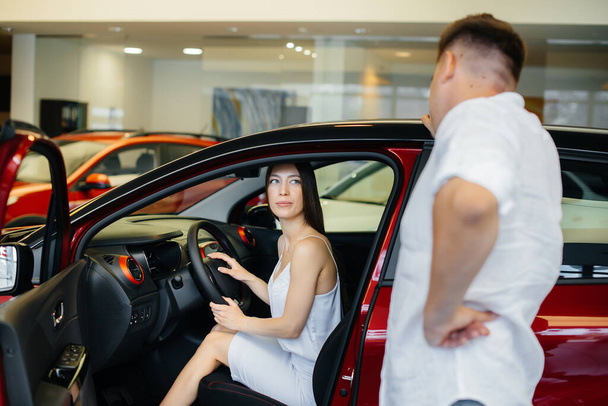 A happy young couple chooses and buys a new car at a car dealership. Buying a new car - Fotó, kép