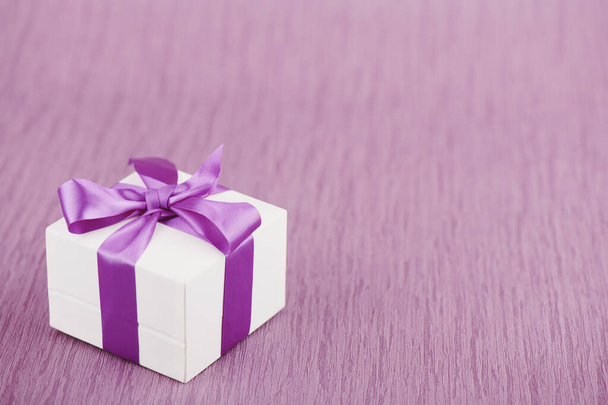 Gift box with purple bow on pink background, shallow depth of sharpness - Photo, image