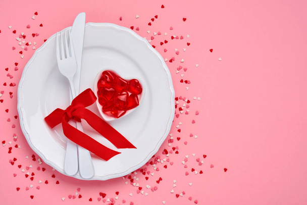 Valentines day background or concept with empty white plate and cutlery fork and knife with red ribbon on pink background. Concept or postcard. Top view flat lay with copy space. - Foto, Bild
