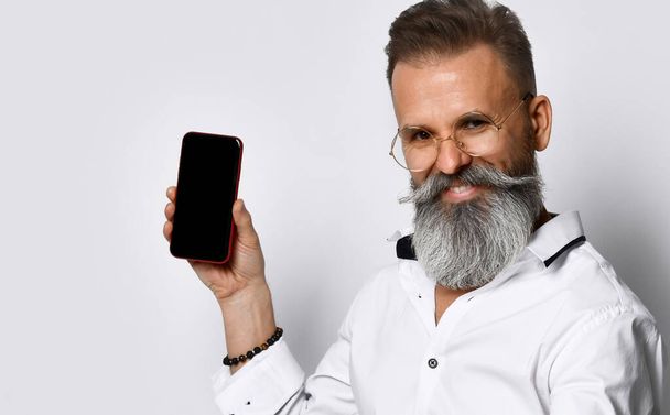 Hipster man with glasses shows the phone to the camera and confidently smiling. - Zdjęcie, obraz
