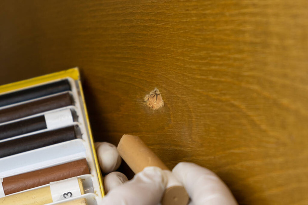 restaurování nábytku, mistr uzavře díru v dřevěném povrchu voskovými tužkami zblízka - Fotografie, Obrázek