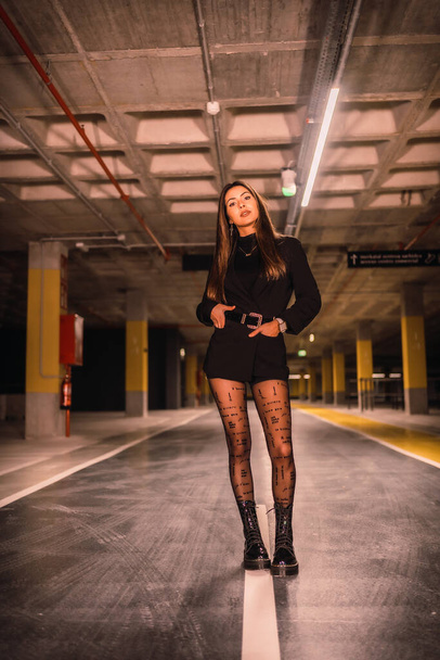 Young Caucasian model on the asphalt of an empty underground car park. Night urban session in the city - Φωτογραφία, εικόνα