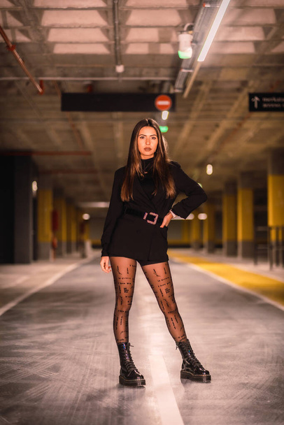 Young caucasian model with black jacket posing in an empty underground car park. Night urban session in the city - Фото, изображение