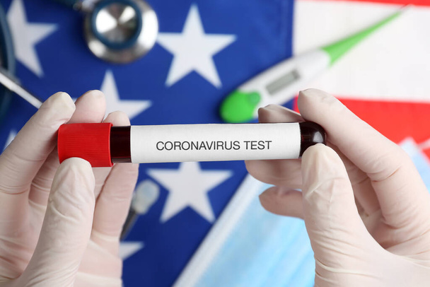 Scientist holding test tube with blood sample over American flag, closeup. Coronavirus pandemic in USA - 写真・画像
