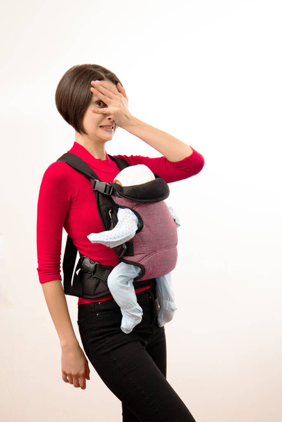 Babywearing confus jeune mère avec bébé dans le transporteur inférieur à la norme. Isolé sur blanc - Photo, image
