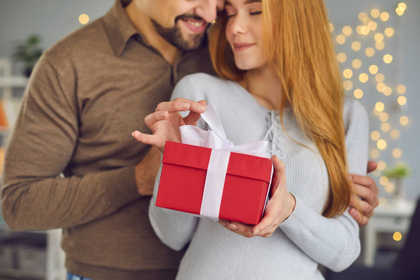 Beautiful loving young couple woman and man hugging and holding red holiday present box with gift - Foto, Imagem