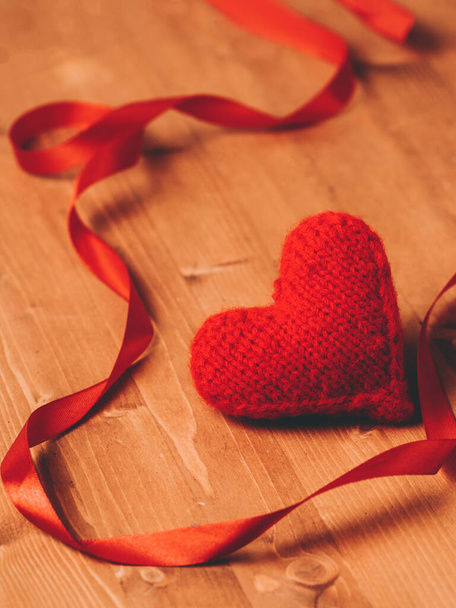 Μια κόκκινη πλεκτή καρδιά και μια κόκκινη κορδέλα σε ξύλινο τραπέζι. Κάρτα του Αγίου Βαλεντίνου - Φωτογραφία, εικόνα