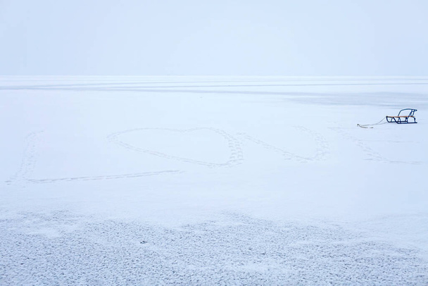 凍結湖の雪の中でハート型の足のパス。冬のロマンチックで氷の風景 - 写真・画像
