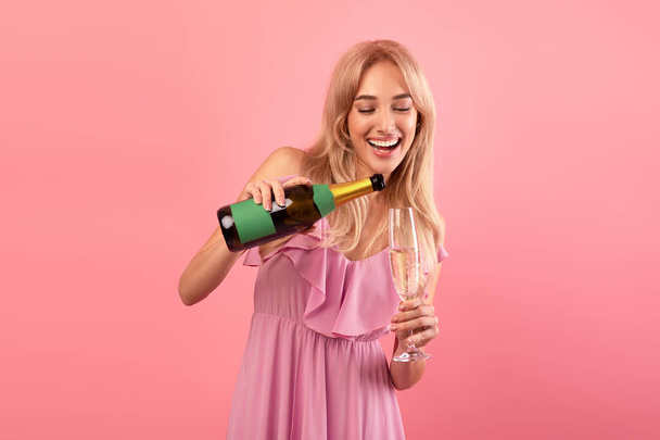 Bájos hölgy öntött pezsgő palackból üvegbe, ünnepli nyaralás, szórakozás party rózsaszín háttér - Fotó, kép