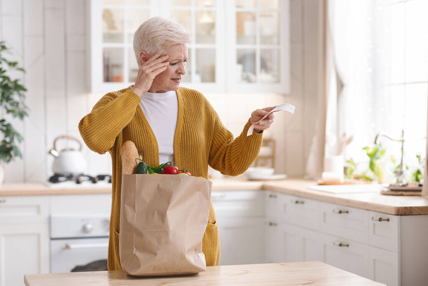 Choqué femme âgée vérifier la facture d'épicerie dans la cuisine - Photo, image