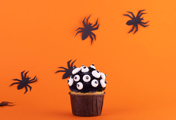 黒のクモのいるオレンジの背景にハロウィーン用のマシュマロの目がたくさん入った黒のカップケーキ。神秘的な恐ろしい背景 - 写真・画像
