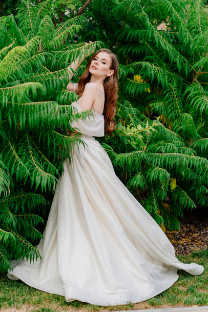beautiful woman in a white dress posing in against of green leaves. - Foto, afbeelding