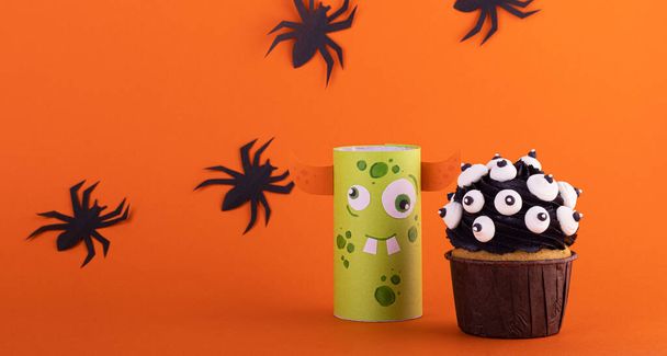 funny paper monster with a scary cupcake on an orange background with black spiders. background for Halloween - Zdjęcie, obraz