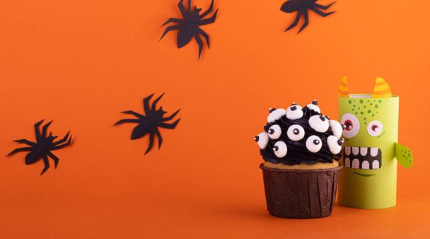 funny paper monster with a scary cupcake on an orange background with black spiders. background for Halloween - Zdjęcie, obraz