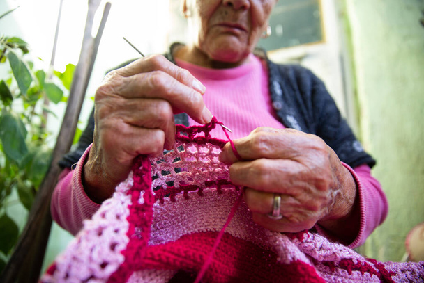 Wieczorem starsza kobieta robi na drutach w domu. - Zdjęcie, obraz