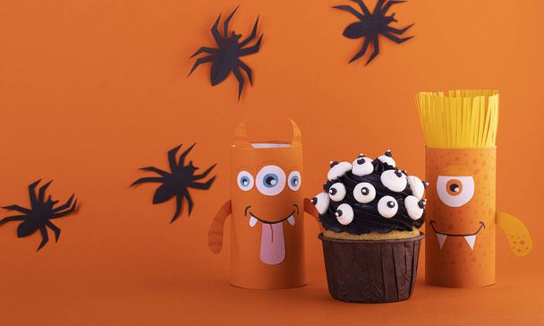 Paper ghost, a scary handmade monster with a black cupcake on an orange background with black spiders. The concept of Halloween crafts, DIY, creative toilet tube - Foto, immagini