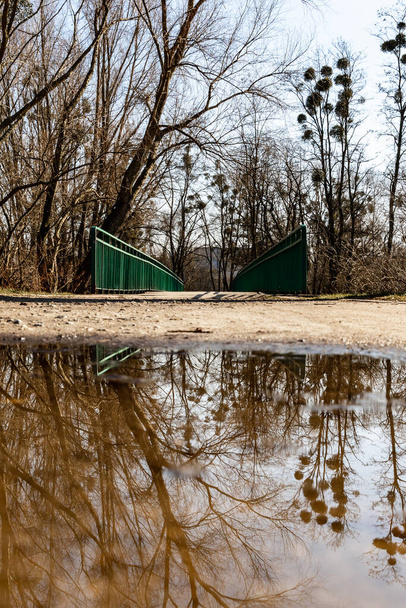 Lange Betonbrücke über den Fluss mit grünem Metallgeländer spiegelt sich in einer kleinen Pfütze - Foto, Bild