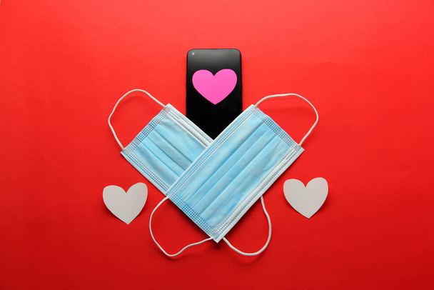 Valentijnsdag in pandemie door covid-19, mobiele telefoon met beschermmasker klinisch gebruik en roze harten - Foto, afbeelding