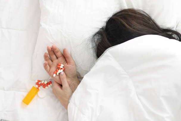 Mão das mulheres se destaca debaixo do cobertor, pílulas jazem em sua mão. - Foto, Imagem