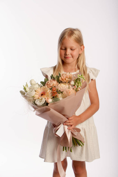 Studio portret van schattig blond meisje in witte jurk met mooi cadeau boeket, witte achtergrond, selectieve focus - Foto, afbeelding