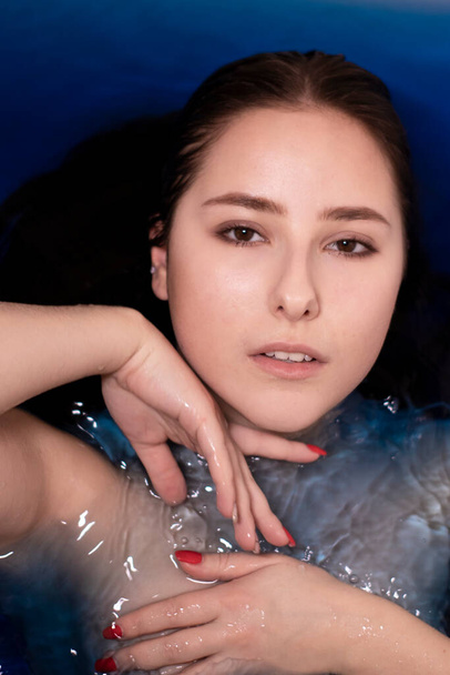 Porträt einer attraktiven brünetten Frau oben ohne in blauer Flüssigkeit. in Badewanne mit farbigem Wasser. Ertrinkendes Mädchen. Kopierraum - Foto, Bild
