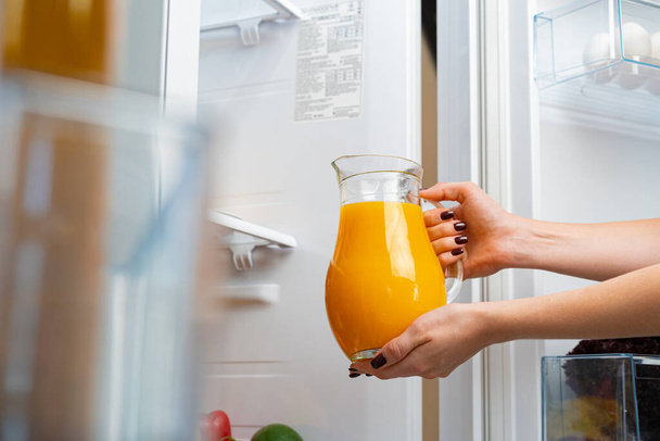 Female hand taking orange juice jar from a fridge - Photo, Image