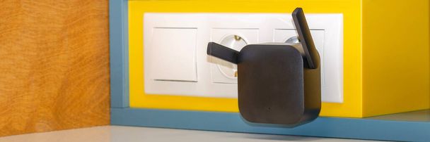WiFi repeater in an electrical outlet on a yellow wall. An easy way to extend your wireless network at home - Photo, Image