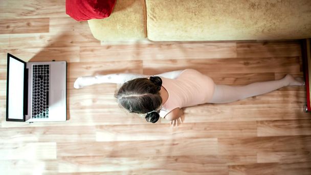 Junge Ballerina in Beinspaltung übt klassische Choreographie während des Online-Kurses zu Hause - Foto, Bild