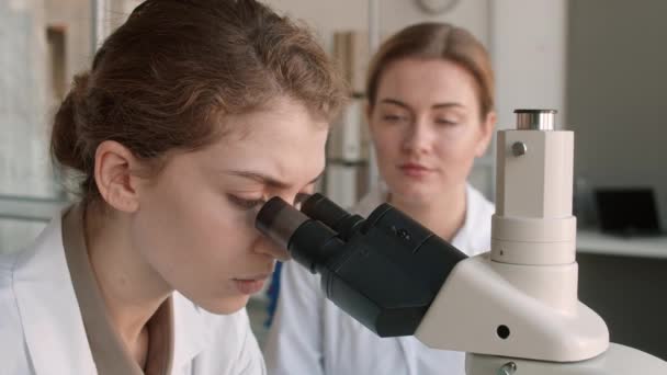 Lockdown of young female scientist sitting at worktop in biochemical lab, using microscope while working on medical research - Footage, Video