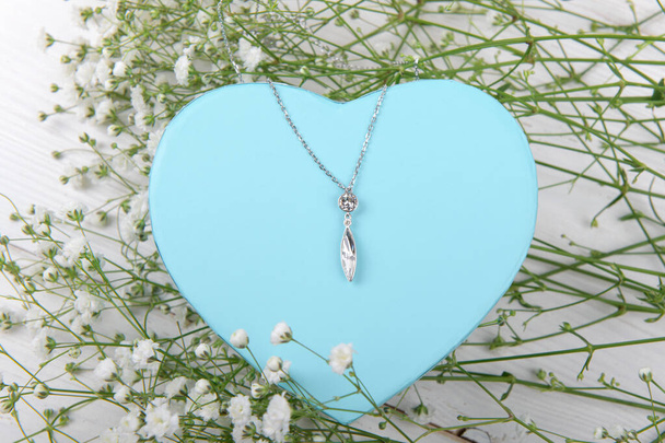 Mavi kalp şeklindeki hediye kutusunda zarif bir kolye beyaz bir arka planda küçük çiçekli, Sevgililer Günü, bayram, evli çiftlerin yıldönümü. - Fotoğraf, Görsel