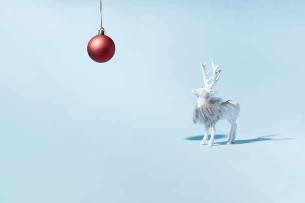 Χριστουγεννιάτικος τάρανδος με κόκκινη λάμπα σε παστέλ μπλε φόντο. Σύγχρονη μινιμαλιστική χριστουγεννιάτικη κάρτα. - Φωτογραφία, εικόνα