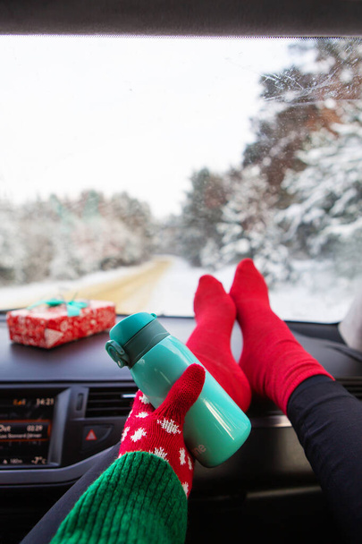 The girl is holding a thermos while sitting in the car in winter, on the background of the winter forest. Travel, trip and winter concept - Photo, Image