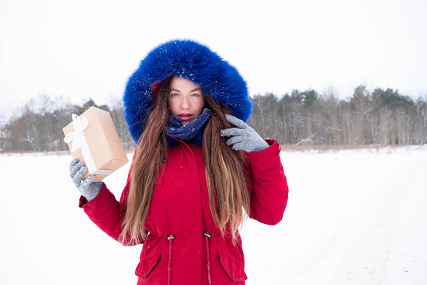 Young serious woman in red hold gift box outdoors - Фото, зображення