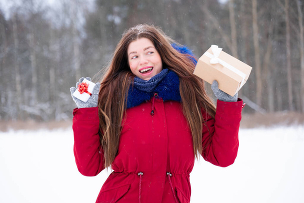 Young smiling woman in red hold gifts outdoors - Фото, изображение