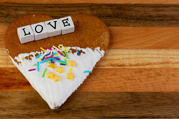 Состав глазурованного имбирного хлеба в форме сердец и слова "Любовь", расположенного на деревянной доске - Фото, изображение